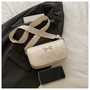 Detail of off-white leather saddle bag with gold bow buckle and wide woven strap