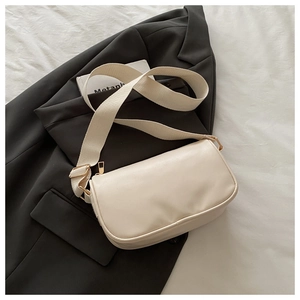 Detail of creamy white crossbody bag with wide fabric strap on a black blazer jacket