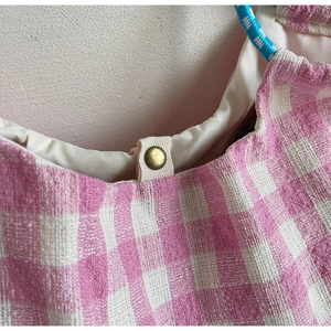 Detail of pink gingham fabric tote bag showing vintage gold snap button and woven handle