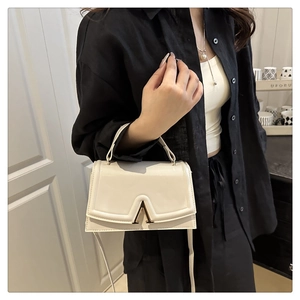 Detail of cream flap handbag with gold V-shaped metal clasp and polished leather texture
