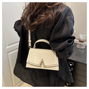 Detail of cream leather crossbody bag with gold V-clasp and adjustable shoulder strap