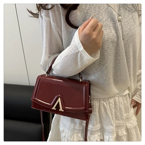 Detail of burgundy glossy handbag with gold V-clasp and elegant metal hardware