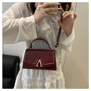 Detail of burgundy crossbody bag with gold V-buckle showing size and leather texture
