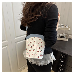 Detail of white cherry print bucket bag with blue straps and golden hardware buckles