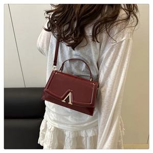 Detail of burgundy patent leather crossbody bag with V-shaped gold buckle worn by model