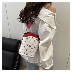 Adjustable geometric woven shoulder strap and red cherry print bucket bag detail
