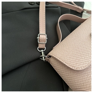 Detail of pink woven leather texture and silver metal hardware on a crossbody bag