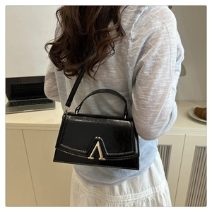 Detail view of the black leather crossbody bag with golden V-logo on a model back