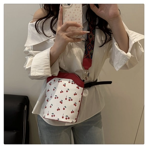 Mirror selfie showing the white bucket bag with red cherry print and woven shoulder strap