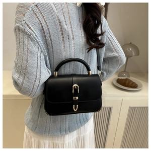 Detail of black leather handbag featuring a golden buckle and adjustable thin shoulder strap