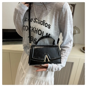 Detail shot of black glossy leather crossbody bag featuring a golden A-shaped metal buckle