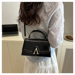 Detail of glossy black patent leather shoulder bag with golden V-shaped buckle