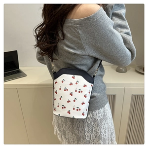 Detail of white bucket bag with cherry print and golden hooks on a model