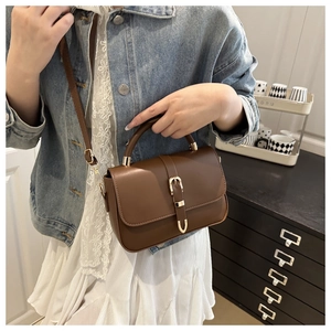 Brown leather handbag with gold horseshoe buckle worn by model in casual style