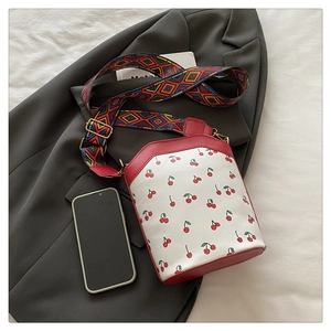 Mini cherry print bucket bag with colorful woven strap compared to a mobile phone