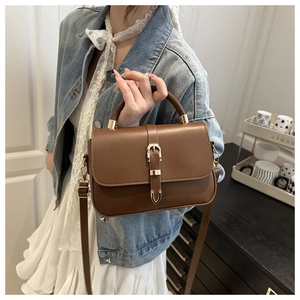 Brown matte leather crossbody bag with metal buckle worn with a casual denim outfit