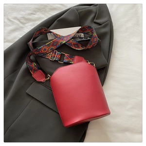 Detail of red PU leather bucket bag featuring a bohemian embroidered wide strap on a blazer