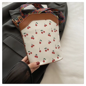 Detail of cherry print tote with brown leather edges and geometric woven shoulder strap