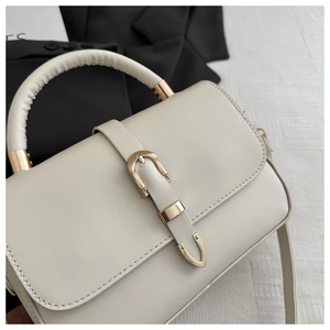 Detail of cream crossbody bag featuring light gold buckle and structured leather handle
