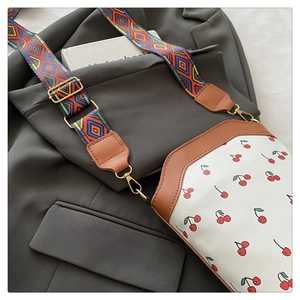 Detail of white cherry print tote bag with brown leather trim and colorful woven strap