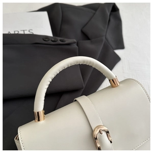 Close-up of beige leather handbag with golden horseshoe buckle and fine stitching