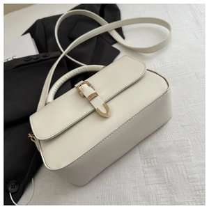 Detail view of cream leather handbag with gold metal lock on white textured fabric background