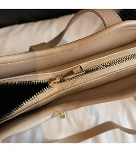 Close-up of smooth gold-tone zipper hardware on a khaki leather tote bag detail
