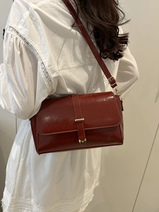Elegant wine red leather shoulder bag with gold heart clasp worn over a white dress
