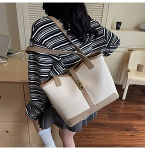 Detail of minimalist tote bag showing contrast straps and turn-lock closure on shoulder