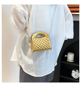 Detail of a shiny gold quilted crossbody bag with a circular handle and elegant metal chain