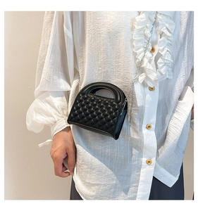Close-up of black quilted leather mini bag with silver chain strap on white shirt