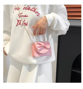 Pink mini crossbody bag with bow and pearl handle shown on model for scale