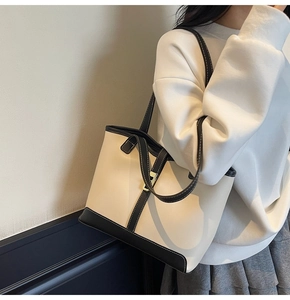 Detail of a cream faux leather tote bag with black contrast trim and gold buckle