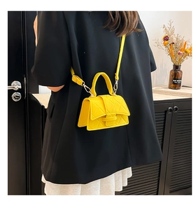 Detail of yellow quilted crossbody bag featuring geometric texture and gold hardware