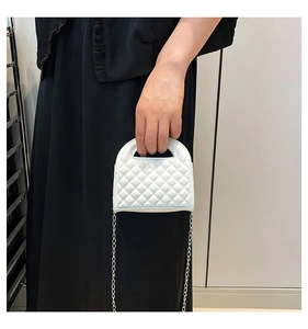 Detailed view of white quilted mini handbag featuring silver chain strap and top handle