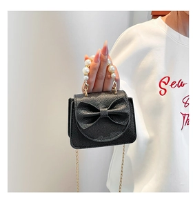 Close-up of black litchi grain leather bag with pearl handle and bow decoration