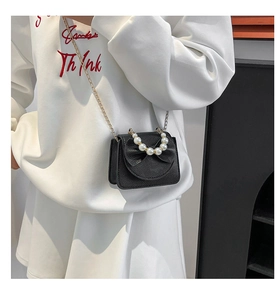 Detail of black pebbled leather crossbody bag with pearl handle and bow decoration
