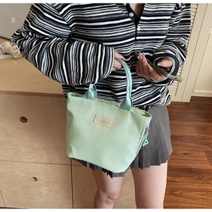 Detail of mint green nylon tote with 'FASHION' label, worn cross-body in a home setting