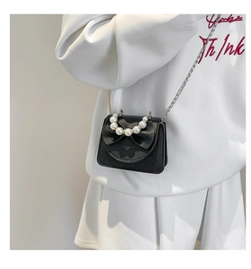 Black mini crossbody bag with a large bow and decorative pearl handle in detail