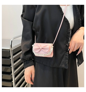 Detail of pink mini crossbody bag featuring leather bow and white lace trim detail