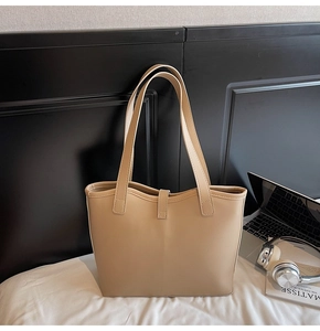 Close-up of beige PU leather tote bag with long handles on white bedding backdrop
