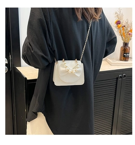 Detail of white mini crossbody bag featuring pearl bow and gold chain strap on model