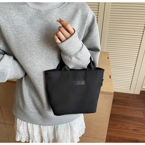 Detail of minimalist black nylon handbag featuring FASHION label and durable webbing handles