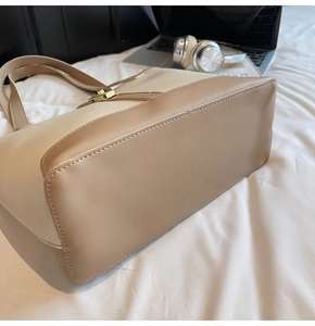 Detail view of reinforced stitching and gold twist-lock on a two-tone leather tote bag