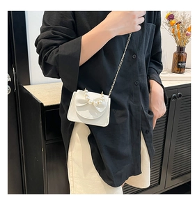 Mini white crossbody bag with pearl bow detail and gold chain strap on model