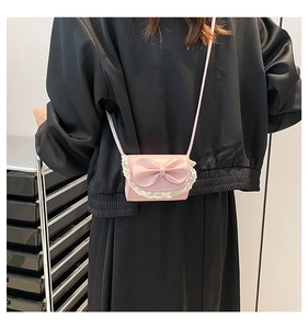Detail of a pink mini crossbody bag with a large bow and white lace trim on a model