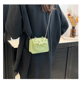 Detail of light green bow shoulder bag with pearl handle and golden chain strap