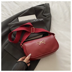 Détail du sac rouge bordeaux avec nœud doré et bandoulière large en toile réglable