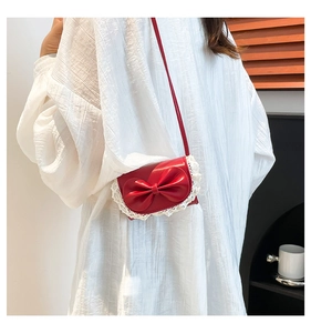 Detailed view of a red bow shoulder bag with white lace trim worn by a model