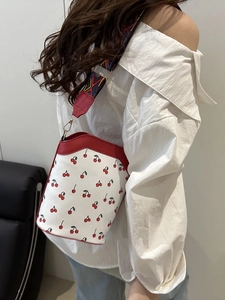 Chic white bucket bag with red cherry prints and colorful woven shoulder strap